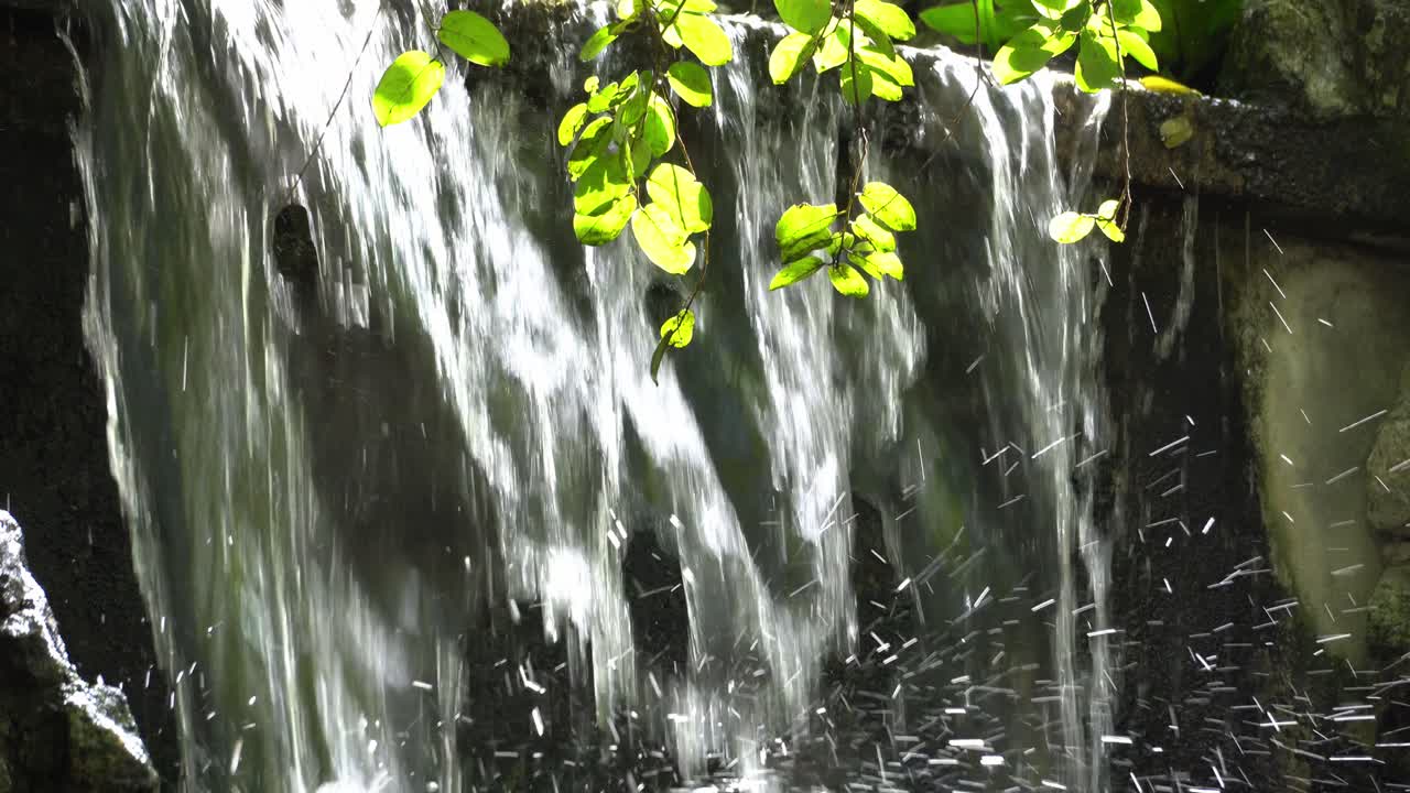 Artificial waterfall with green leaves with sun light