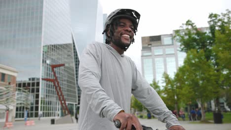 Young-African-American-male-poses-on-his-bike-in-front-of-downtown-buildings-and-park