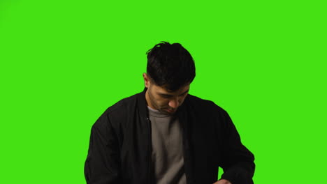 Young-Man-Answering-Call-On-Mobile-Phone-Standing-Against-Green-Screen-Studio-Background-1