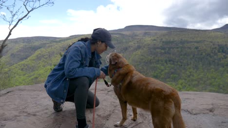 young diverse girl hiker petting loving hugging and kissing on her older dog at hiking trail head view area overlooking waterfall and tree covered mountains in upstate new york 4k slow motion