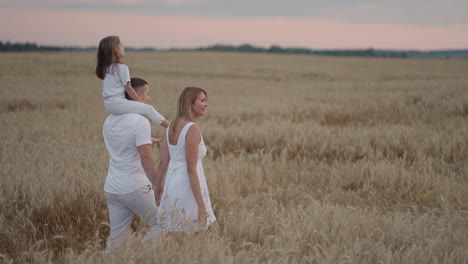 slow motion: happy family of farmers with child are walking on wheat field. healthy mother father and little daughter enjoying nature together outdoors.