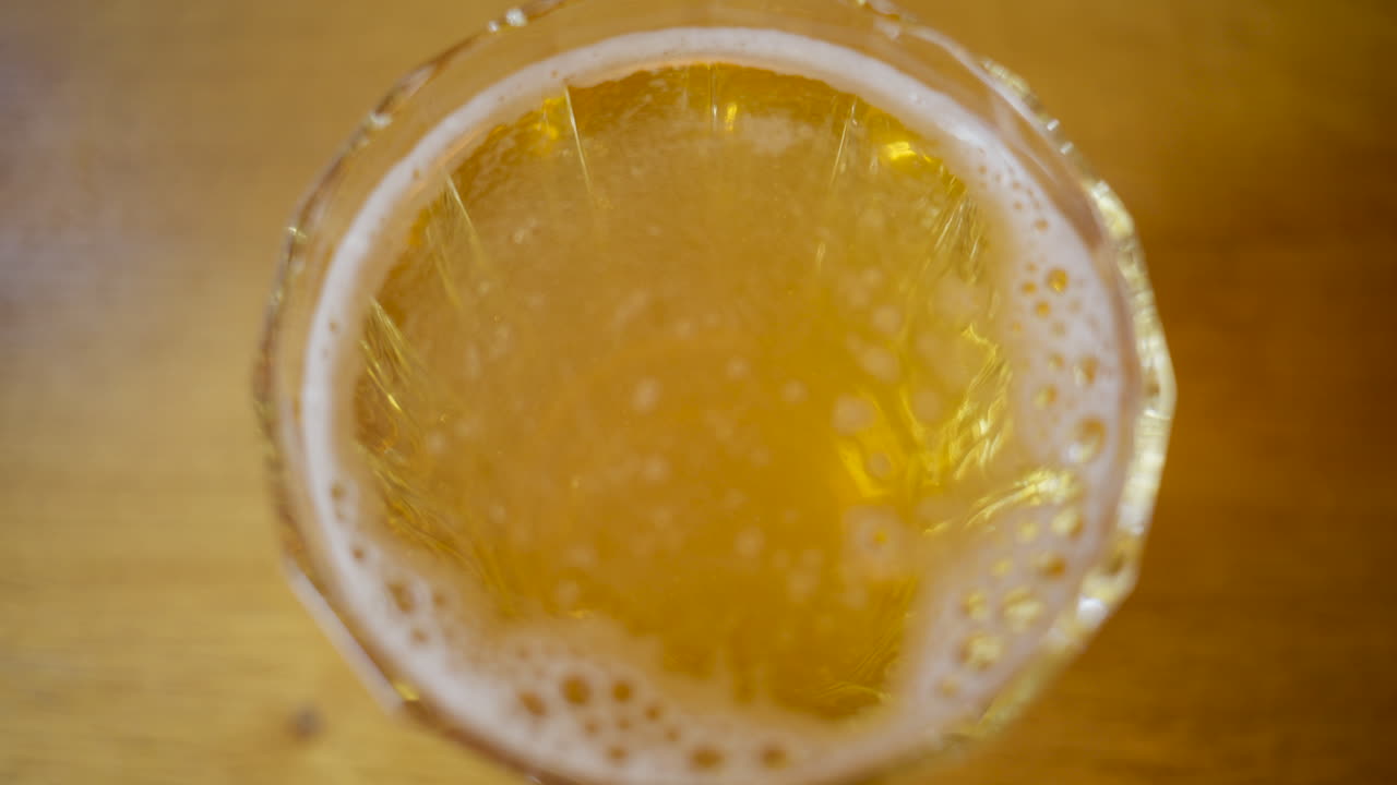 Vista dall'alto di un bicchiere di birra lager chiara appena versata con schiuma su un tavolo di legno.