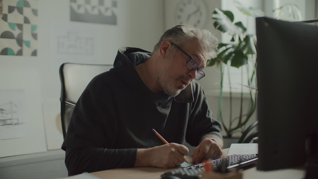 Architect Taking Notes and Using Computer during Phone Call in Office