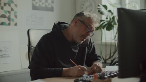 architect taking notes and using computer during phone call in office