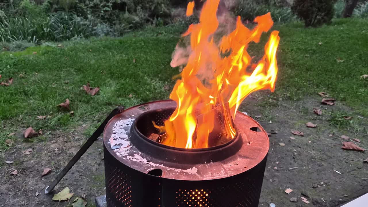 Orange flames dancing in a metal fire pit surrounded by grass, outdoor evening setting
