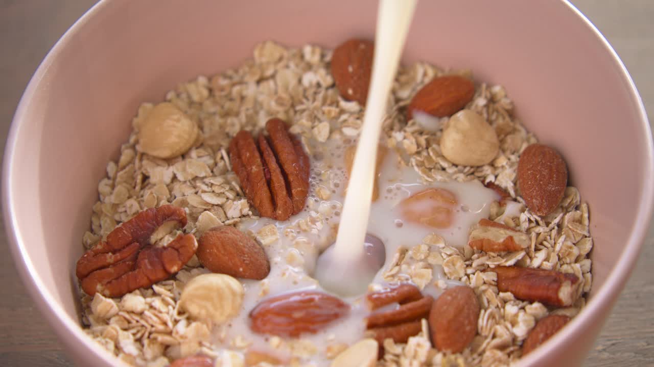 leche vertida sobre un tazón de desayuno saludable, nueces y avena.