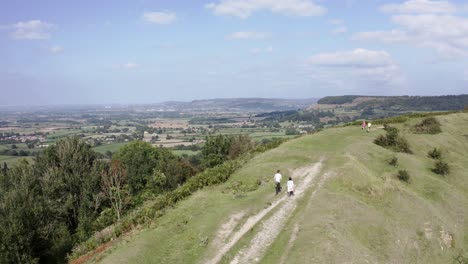 Antenne---Paar-Geht-Mit-Seinem-Hund-Auf-Einem-Hügel-In-Der-Nähe-Von-Uley,-Cotswolds,-England,-Vorwärts