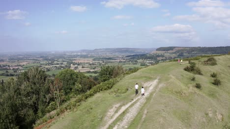공중 - 부부는 uley, cotswolds, england, forward 근처의 언덕에서 개를 산책시킵니다.