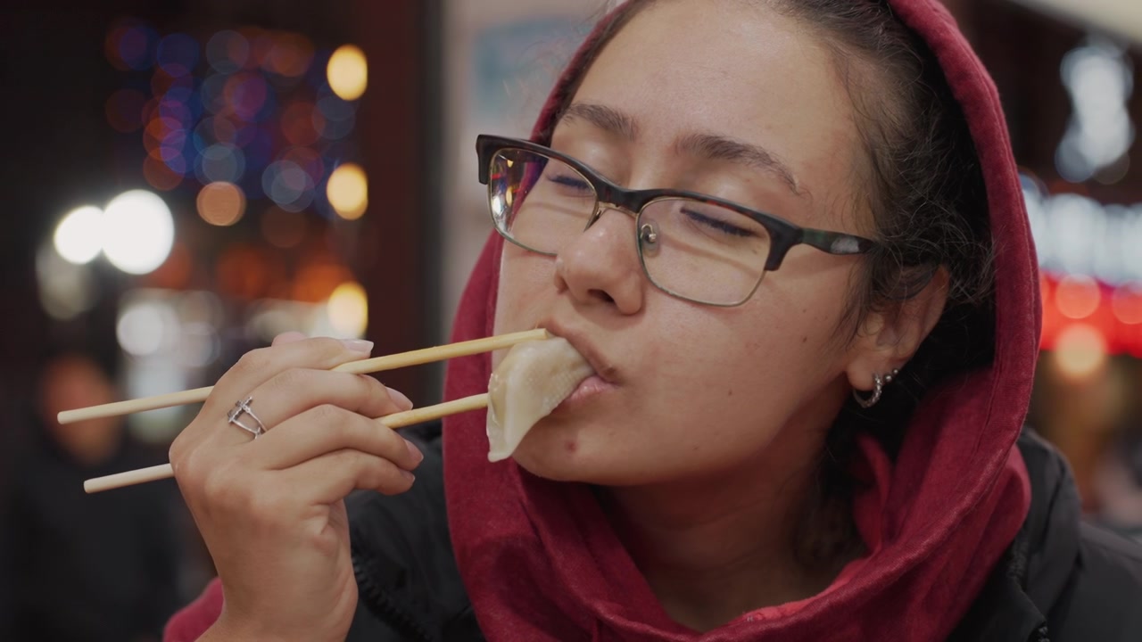 Evening food enjoyment. Woman relishes spicy street snacks. Nighttime market serving flavorful steamed dumplings. Woman enjoys tasting spicy street foods at night market scene