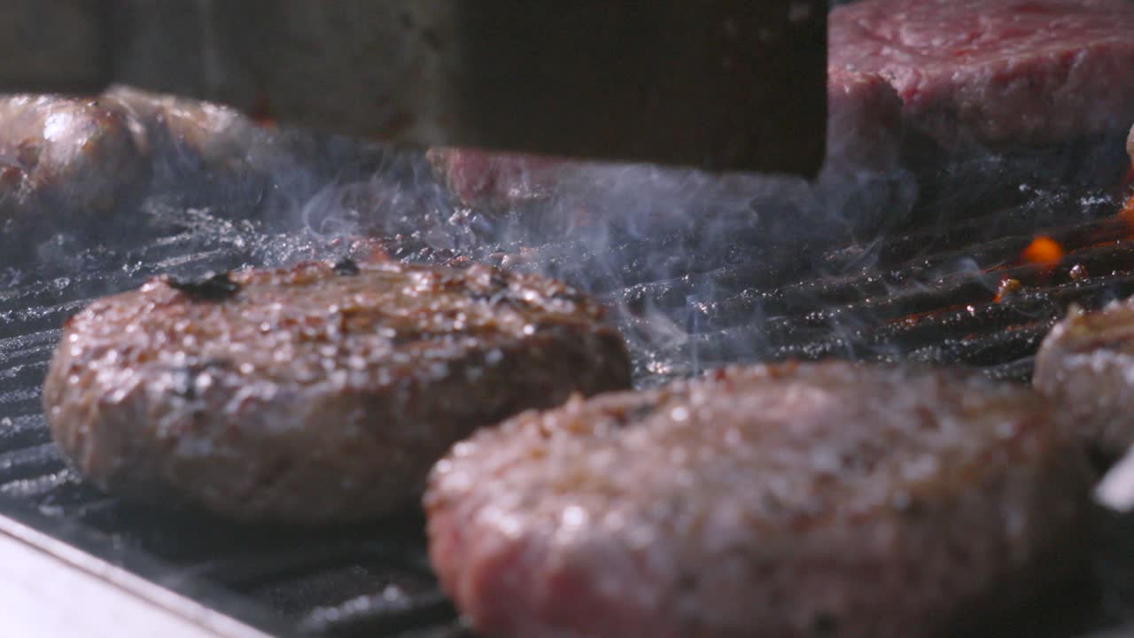 Raw Beef Patties Being Cooked on Iron Grill BBQ with Smoke Rising from Hot Charcoals. Barbecue Tasty Social Food for Lunch or Dinner. High Protein Summer Meat Cooking on Fire Flames.