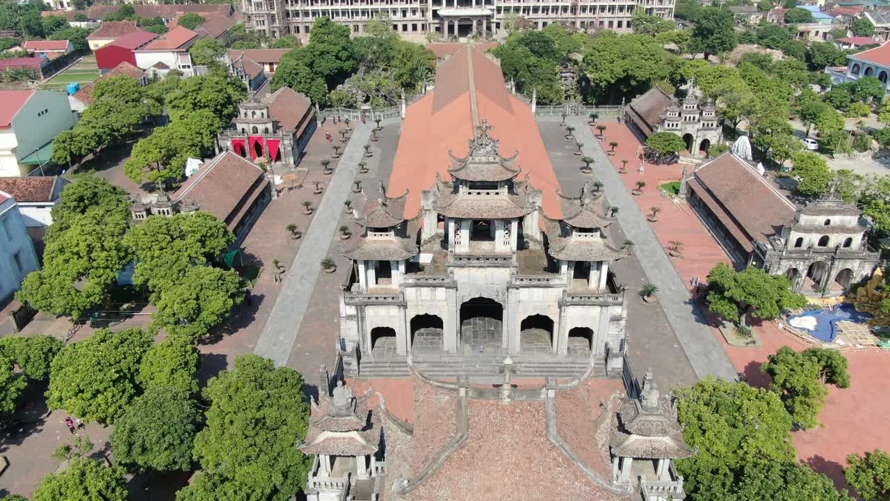 Drone aerial view in Vietnam flying over a stone temple in Ninh Binh on a town with brick roof buildings on a sunny day