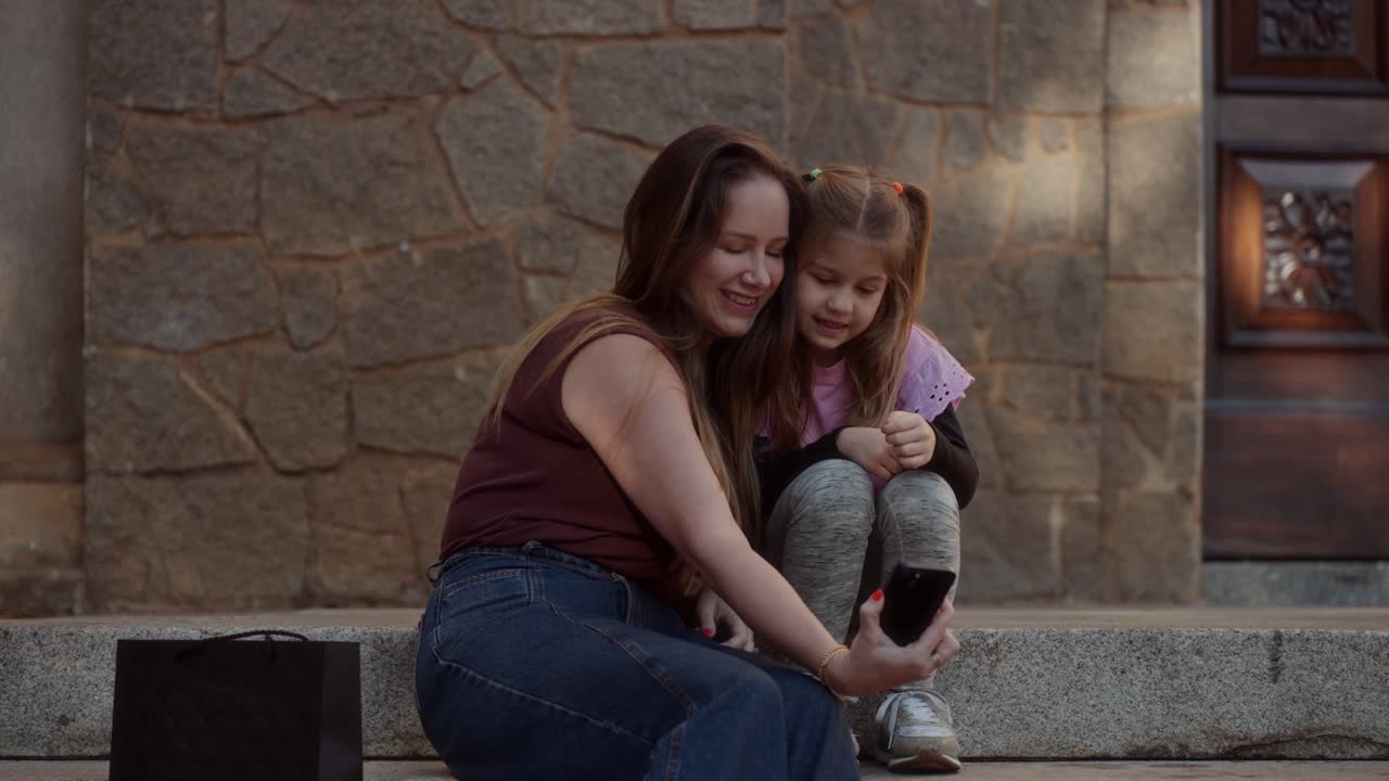 Mother and daughter interacting with a smartphone on stone steps