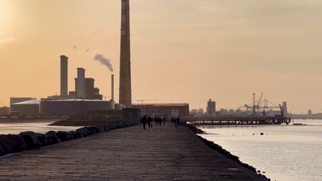 Golden-Hour-Stroll:-Dubliners-Walking-Along-the-Great-South-Wall-with-Poolbeg-Towers,-Ireland