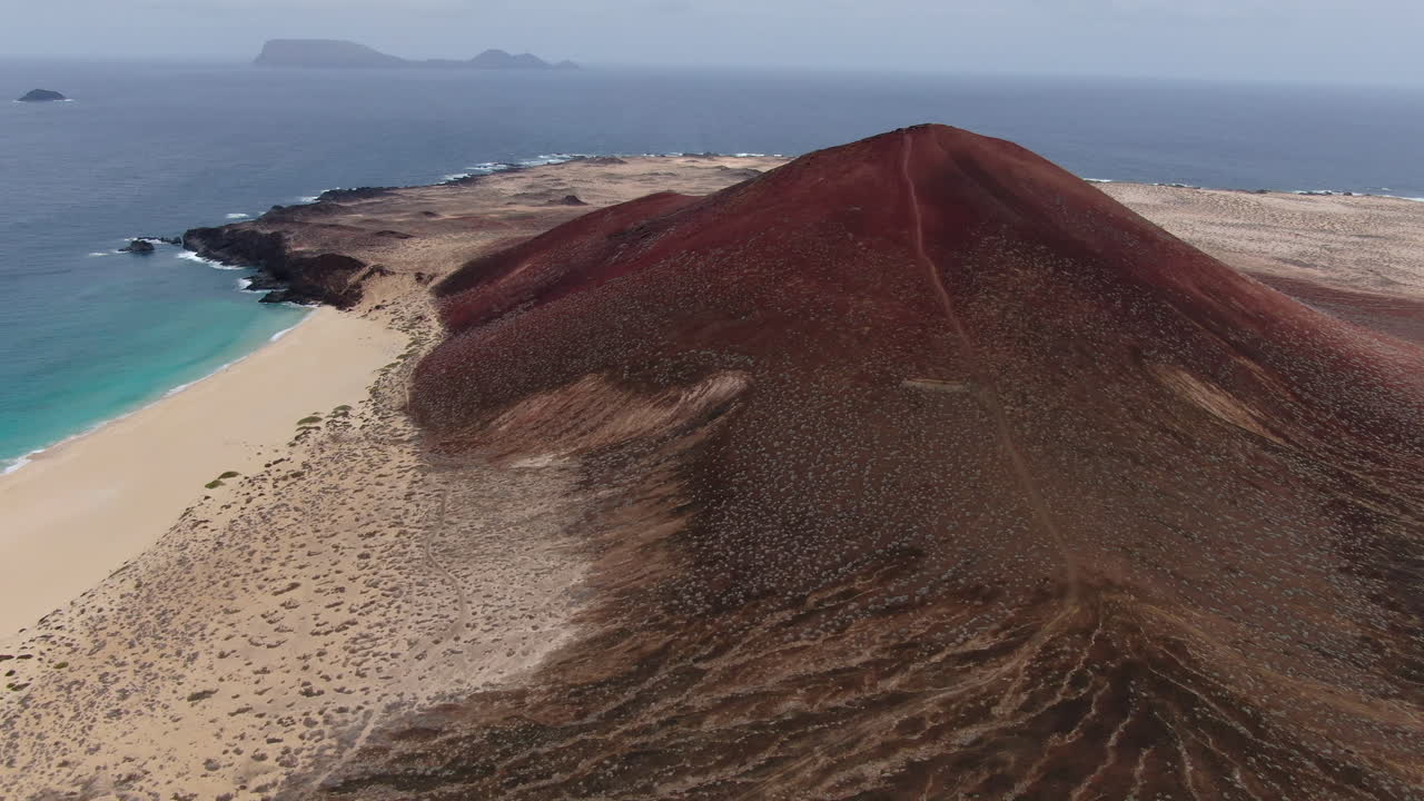 La Graciosa island: aerial view traveling in to the Bermeja mountain and Las Conchas beach on a sunny day and turquoise waters