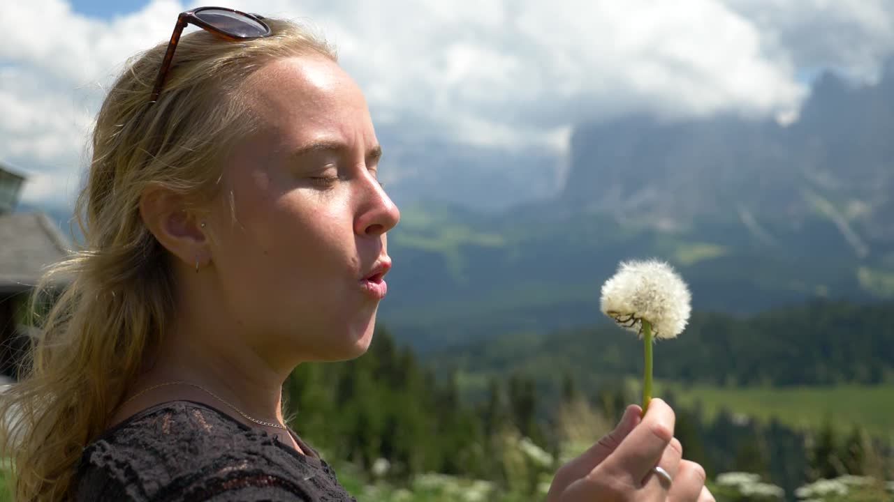 Superslowmotion av en kaukasisk kvinnlig modell som blåser en maskrosblomma mot vinden, Seiser Alm, Val Gardena, Sydtyrolen.