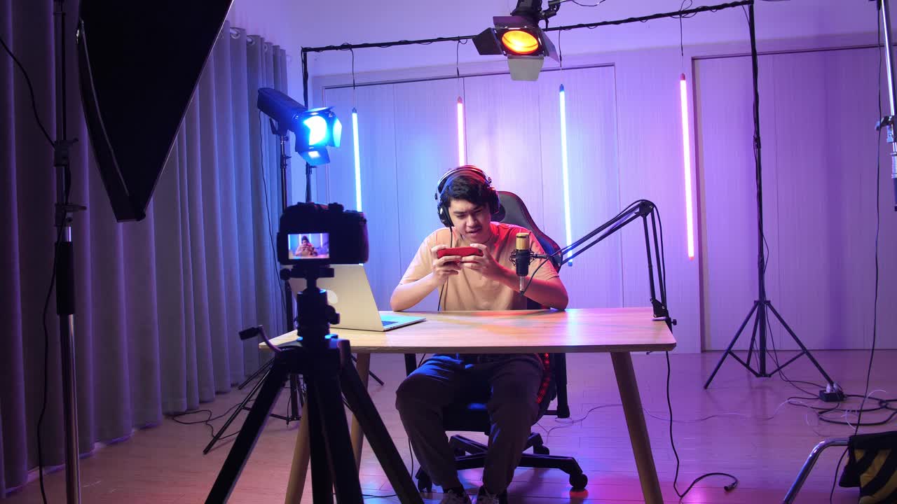Excited Asian Man Playing Video Game With Mobile Phone While Live Stream With Camera, Professional Light Equipment