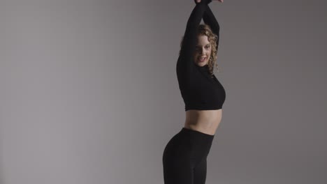 three quarter length studio shot of young woman doing dance practise against grey background