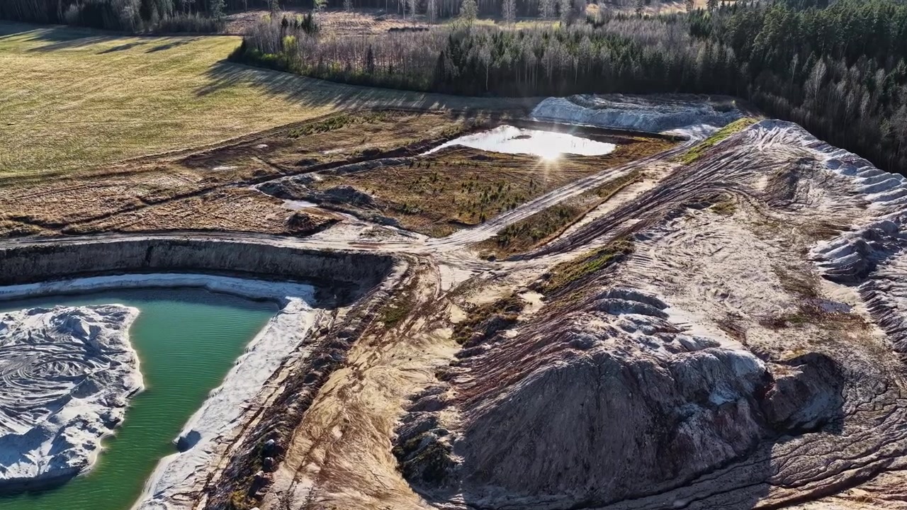 Drone footage of an open pit mine with sand heaps and a green artificial lake