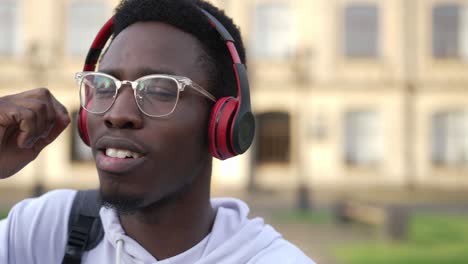 retrato en primer plano de un hombre afroamericano feliz y satisfecho con auriculares bailando en cámara lenta mirando a la cámara disfrutando de la música. fotografía de un estudiante confiado y alegre con gafas posando para divertirse.