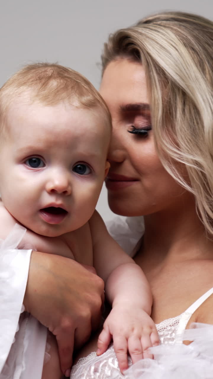 Beautiful Caucasian blonde lady with her adorable little baby. Happy mother with her beloved son at studio. White backdrop. Vertical video