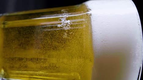 semi-close-up static shot of fresh beer carbonating and foaming against black background, vertical shot