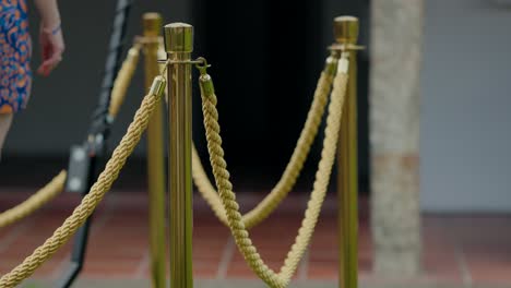postes dorados con cuerdas, que marcan una entrada en un evento, sugiriendo exclusividad y elegancia