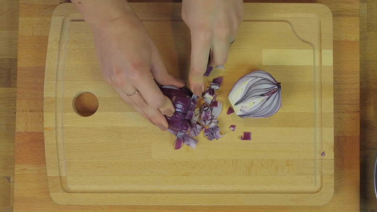 Persona che taglia a cubetti una cipolla rossa su un tagliere di legno