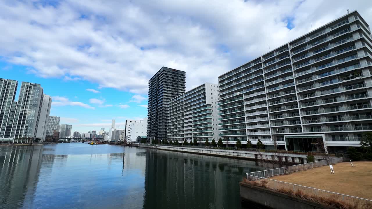 A calm canal in Tokyo with modern skyscrapers, a boat, and a partly cloudy sky
