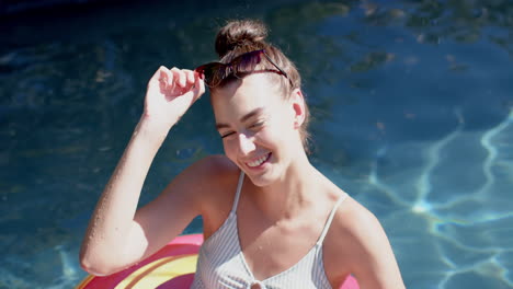 Teenage-Caucasian-girl-with-a-striped-swimsuit-smiles-while-adjusting-her-sunglasses