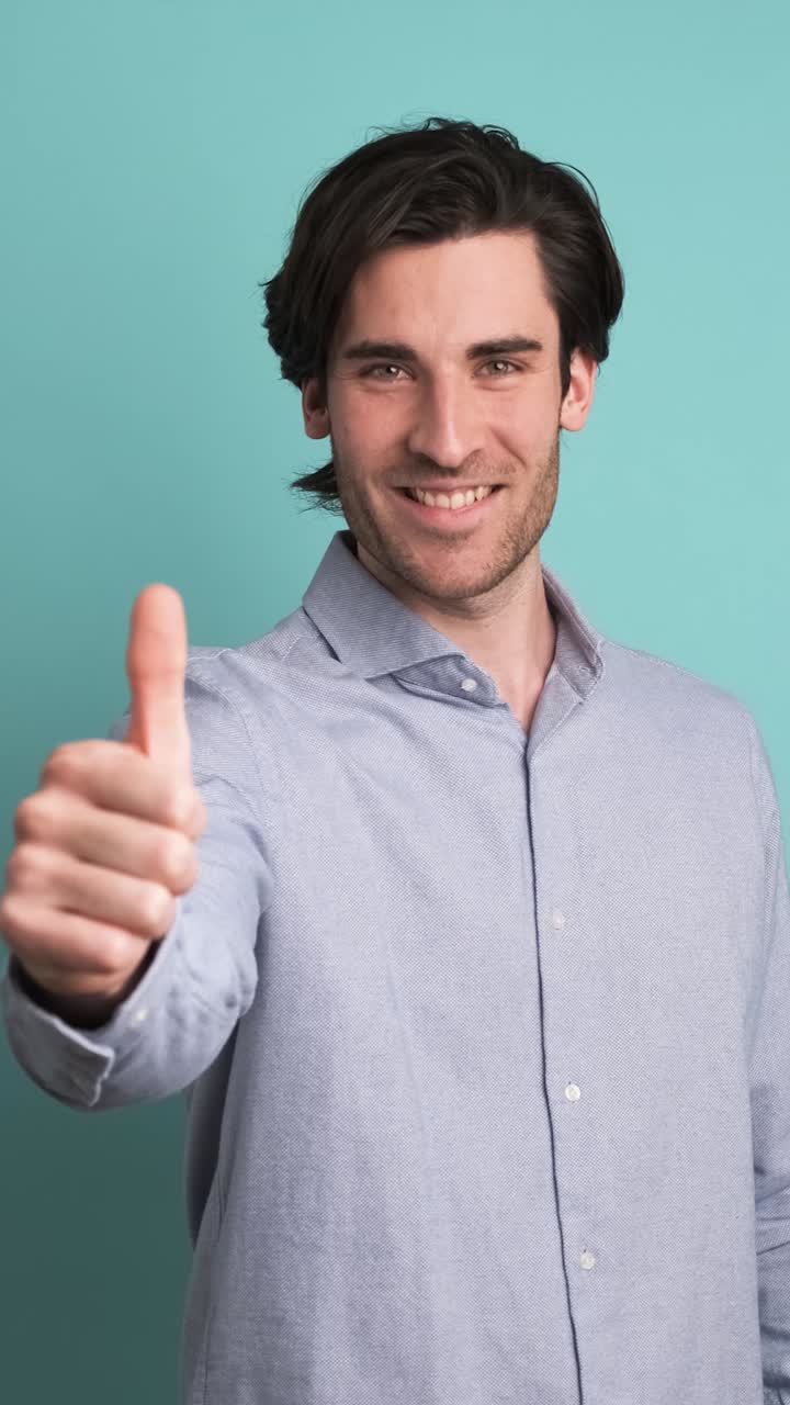 Happy man showing thumbs up in blue studio