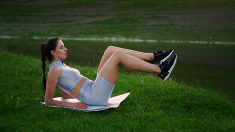 in the morning in the park a woman in sports clothes lying on a mat raises her legs to the body exercise bike. exercises for a beautiful body. the abdominal muscles