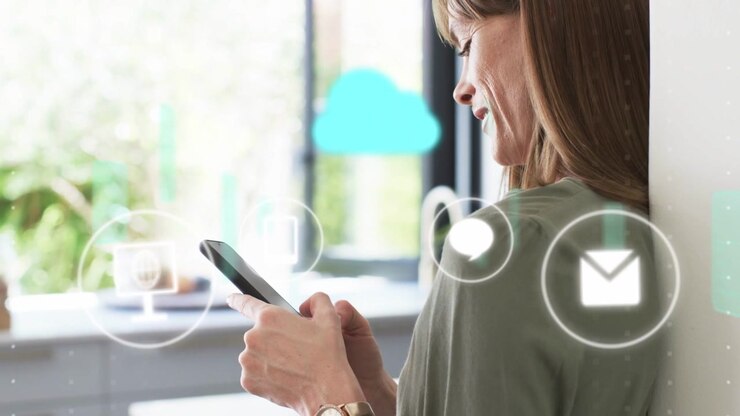 Mid adult woman leaning, tapping smartphone and causing icons floating over phone for tech demo