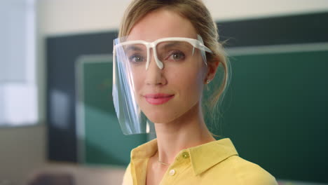 Smiling-schoolteacher-standing-in-classroom.-Woman-wearing-face-shield