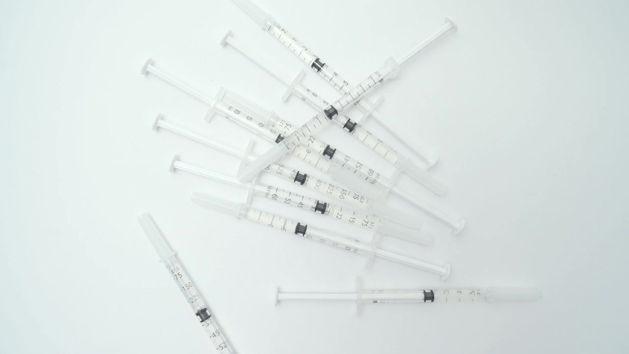 Pila di siringhe nuove e non utilizzate che cadono su uno sfondo bianco isolato, a rappresentare un trattamento medico.