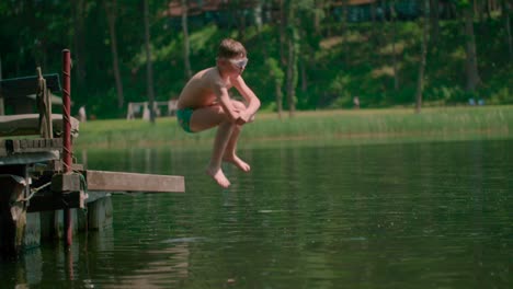 caucasian kid jumping from the wooden pier into the lake