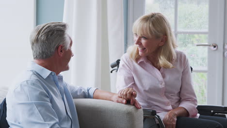 senior couple with woman in wheelchair sitting in lounge at home talking and laughing together