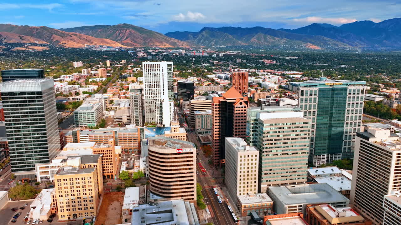Salt Lake City, USA, 14 August 2025: Footage over the tops of the high-rise buildings in the downtown of Salt Lake City, Utah, USA. Stunning mountains range at backdrop