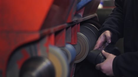 male cobbler working at his shoe repair shop, using craft grinder machine, polishing shoe heel and sole