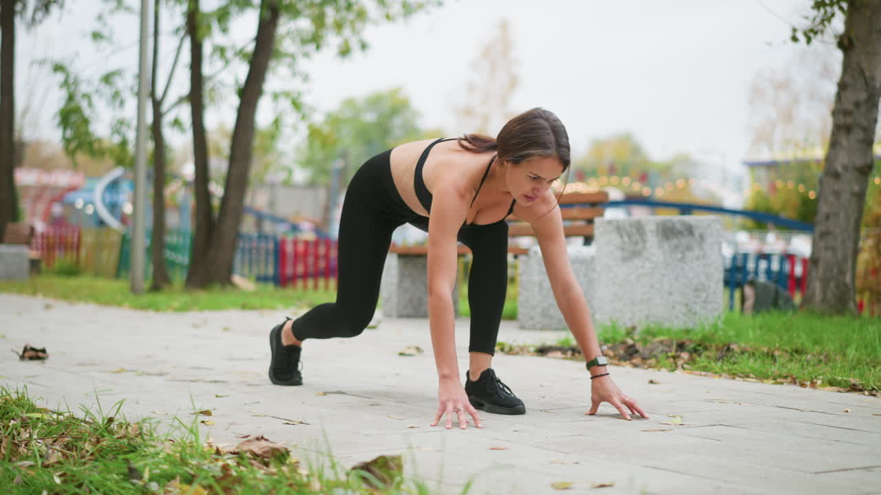 Young woman preparing to run in outdoor park playground, placing hand on ground, athletic fitness, active lifestyle, exercise training, ready to take off for a sprint