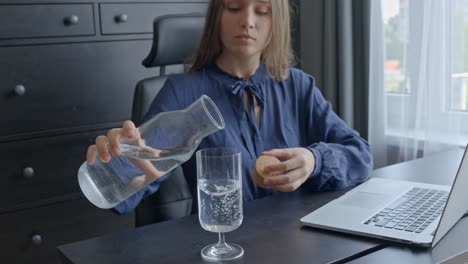 бизнесменка наливает воду в стакан, работая за своим офисом.