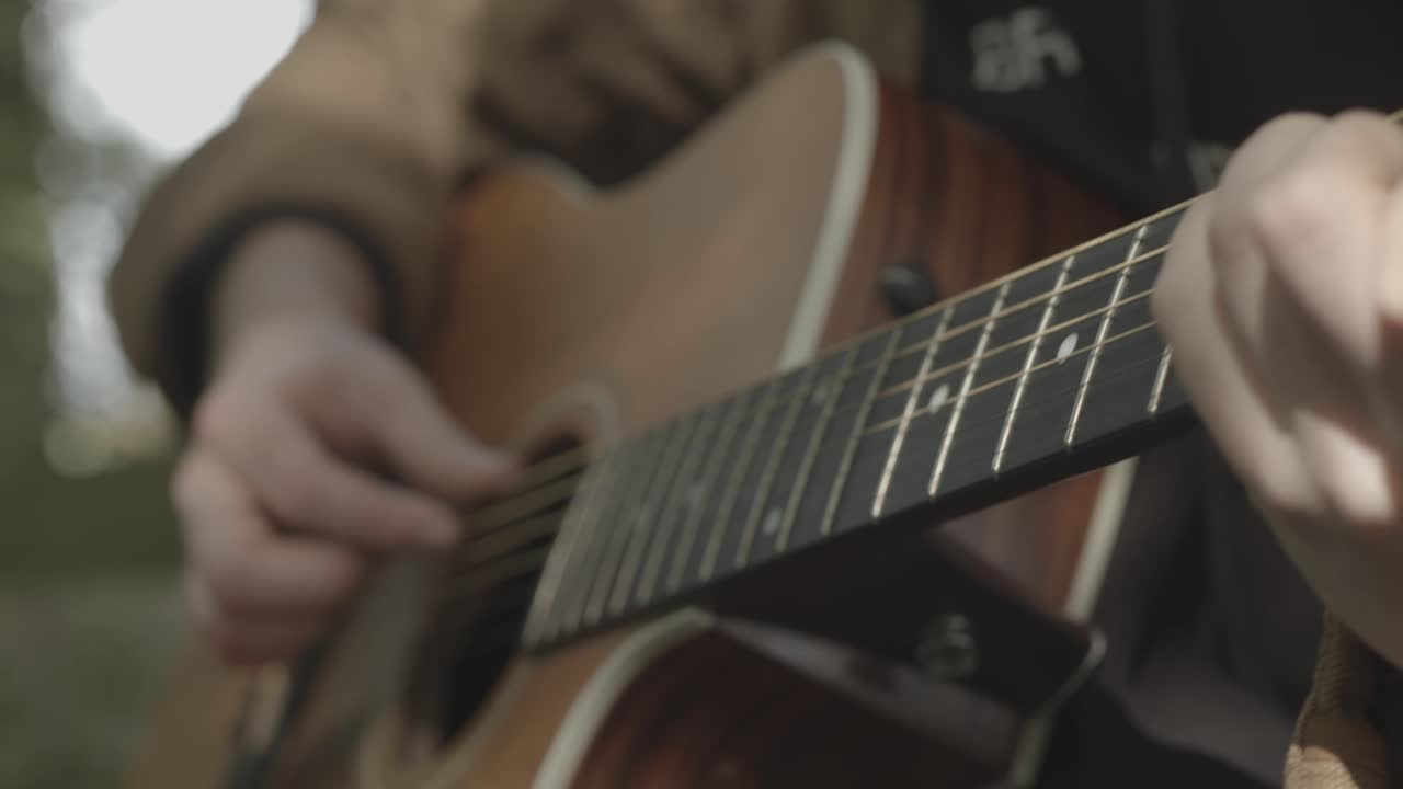 las manos tocan la guitarra acústica con fondo exterior de enfoque suave, cierre de mano