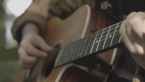 las manos tocan la guitarra acústica con fondo exterior de enfoque suave, cierre de mano