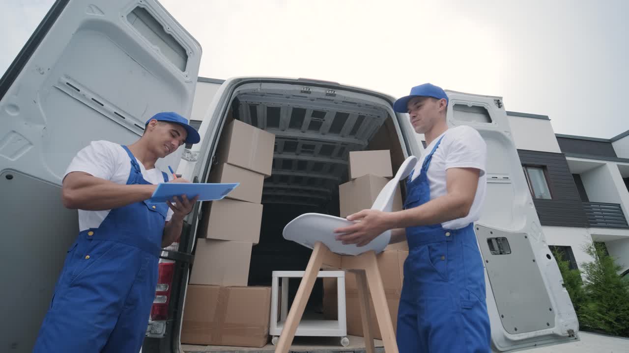 dos jóvenes trabajadores de una empresa de mudanzas descargan cajas y muebles del minibús en la casa del cliente