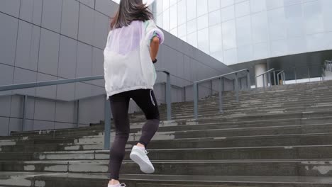 latina millennial girl running up stairs during her workout routine at a modern urban city, seen from behind