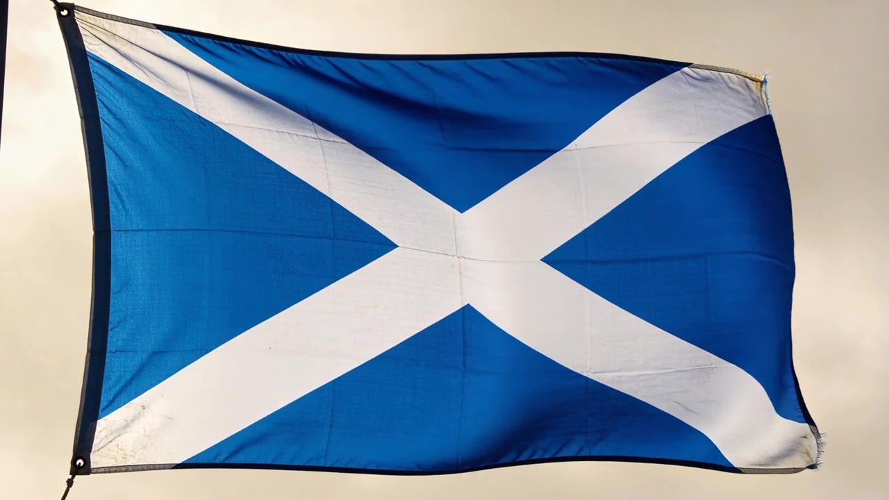 Lieve brezza che fa sventolare la bandiera Saltire blu, arricciandosi e appiattendosi sull'occhiello di issaggio sotto un cielo pallido