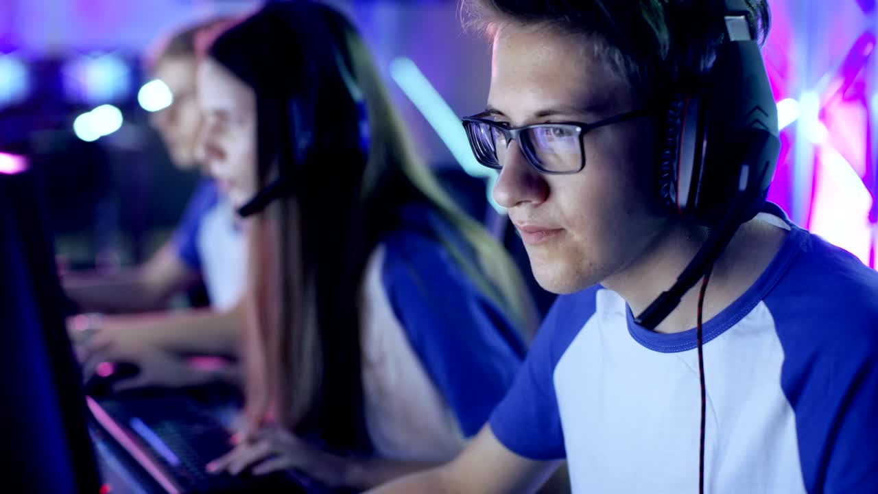 Professionel ung gamer spiller videospil på et e-sportstævne/internetcafé. Han bærer briller og hovedtelefoner og taler i mikrofon.