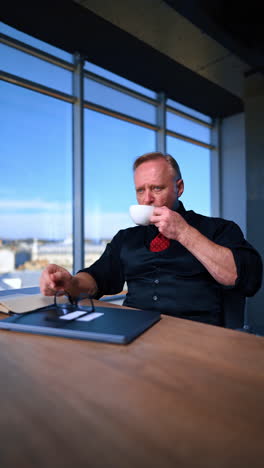 adult bearded man sits at desk in the office. man drinking from a white cup during the break at work. vertical video.