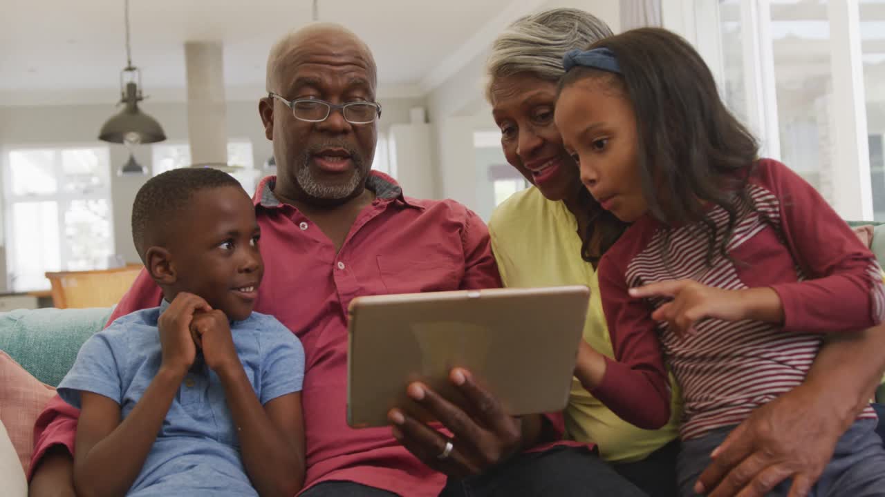 Video of happy african american grandparents and grandchildren using tablet together