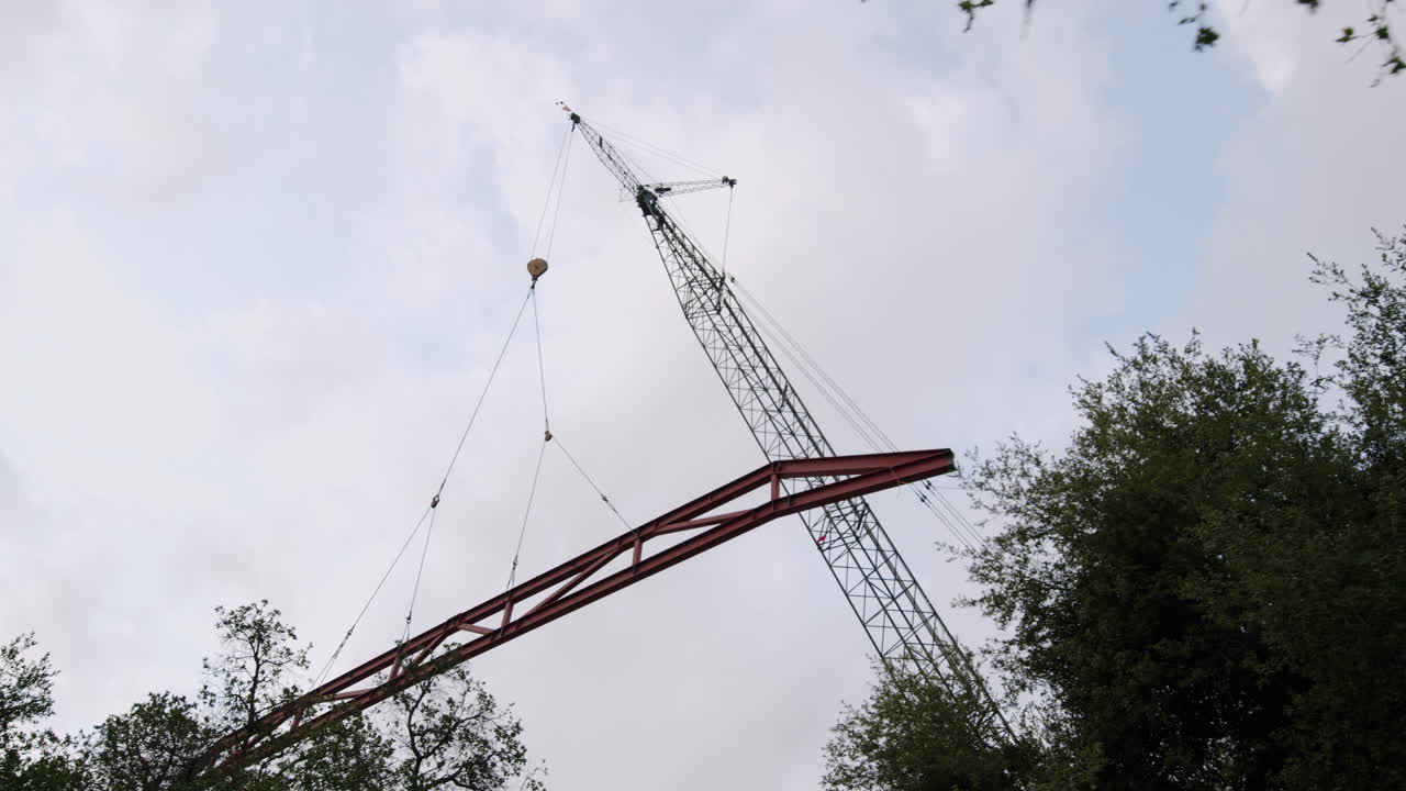 A large crane lifting a metal beam against a cloudy sky