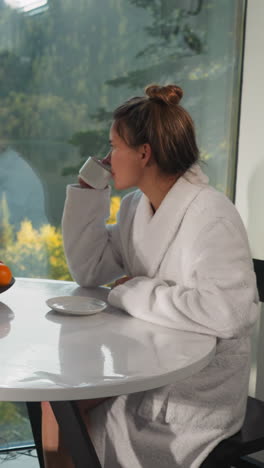 pareja bebiendo té mirando por la ventana panorámica. mujer y hombre pensativos en túnicas de baño pasan la mañana juntos. mañanas tranquilas con café con sabor